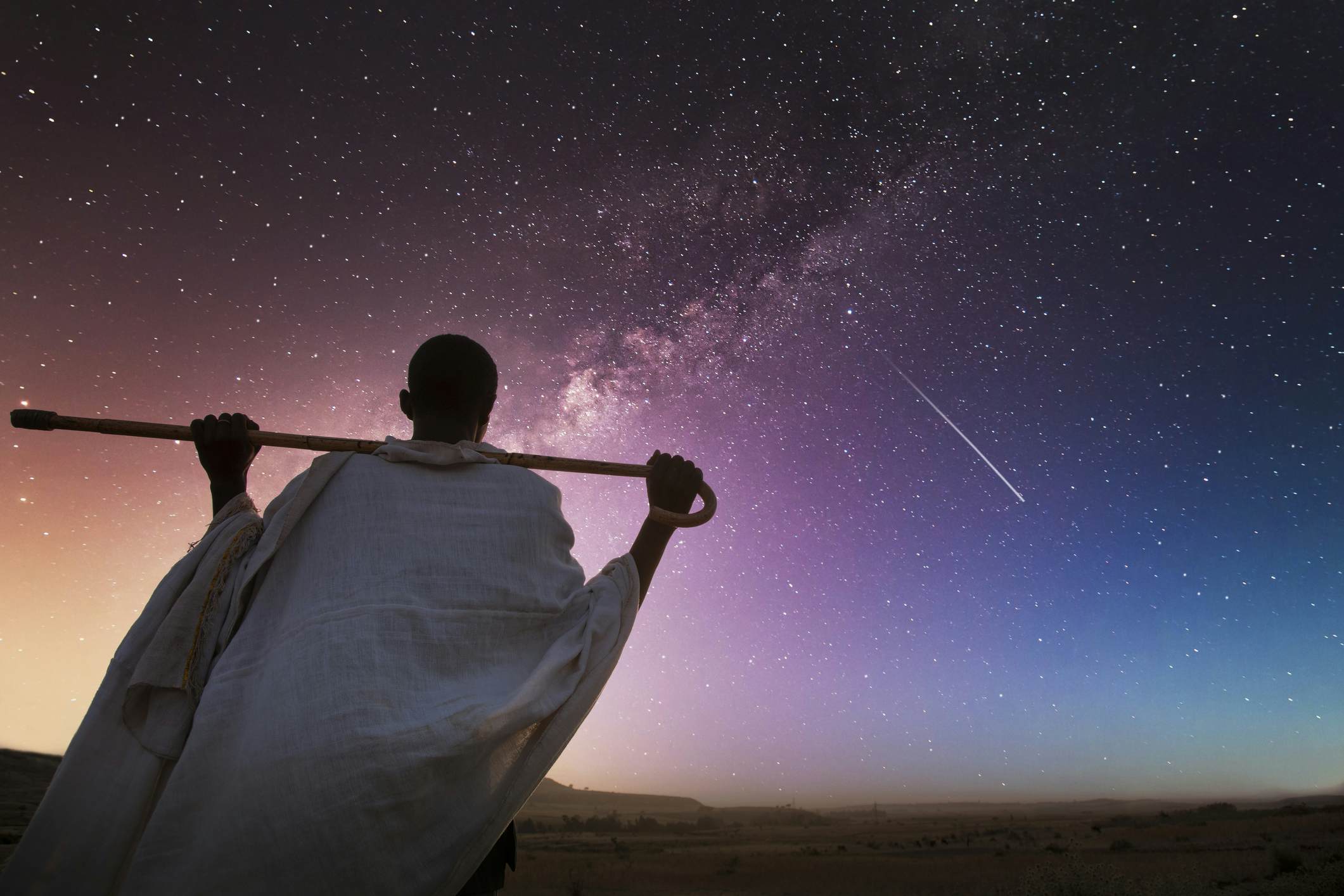 Ethiopia. Rear view of a senior ethiopian man carrying his stick over his shoulder and watching the milky way in a starry sky.